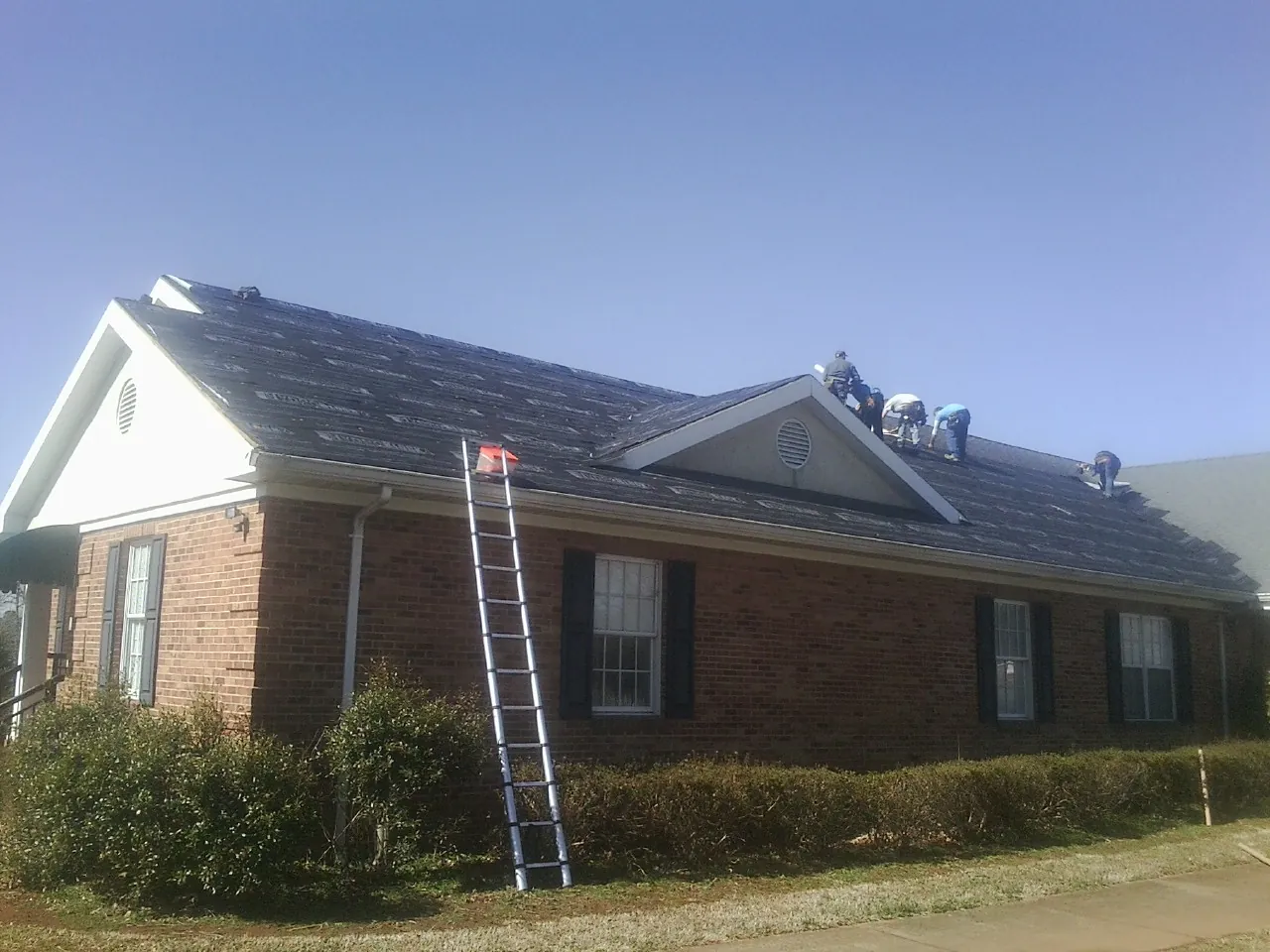 Crew tearing shingles off a brick ranch roof with a ladder set — Metal Roof Repair work by our crew in Pocasset