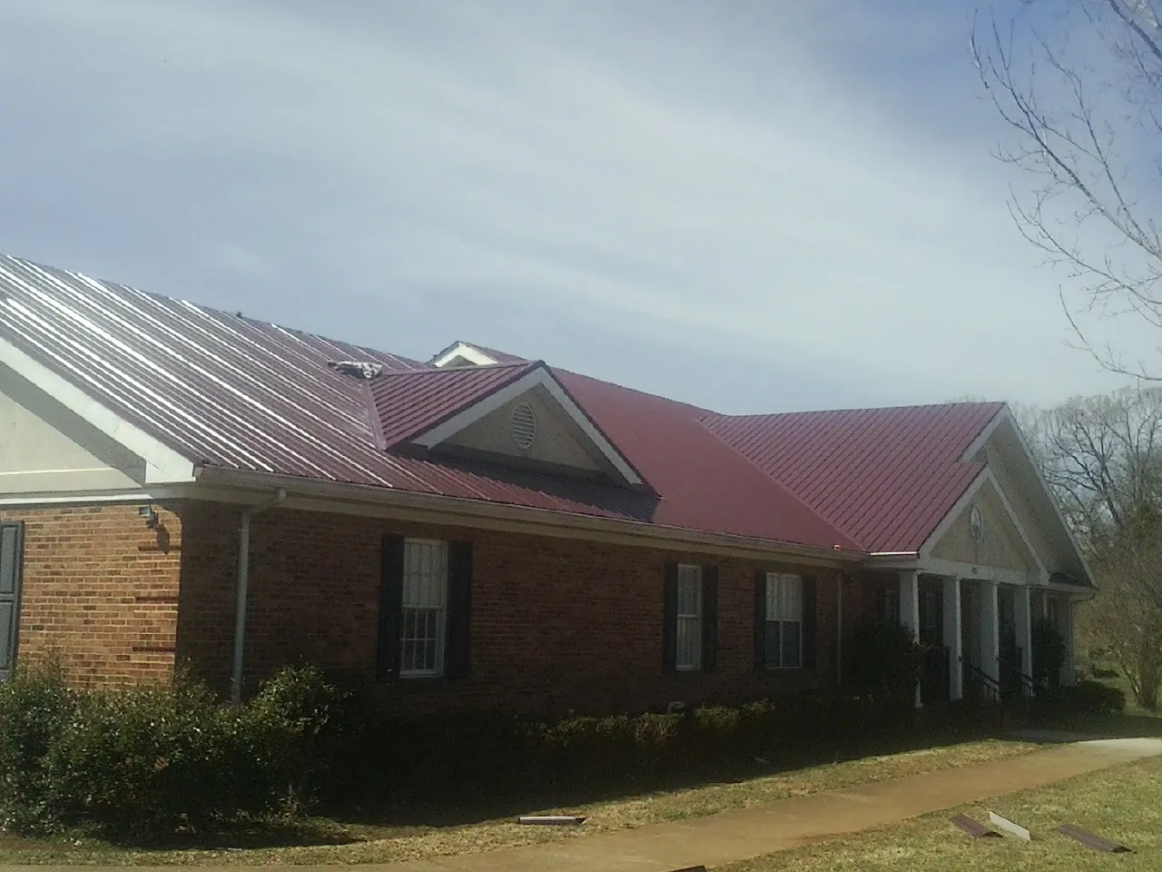 Red metal roof with gabled entries on a long brick building, from a Hail Damage Roof Repair job in Pocasset